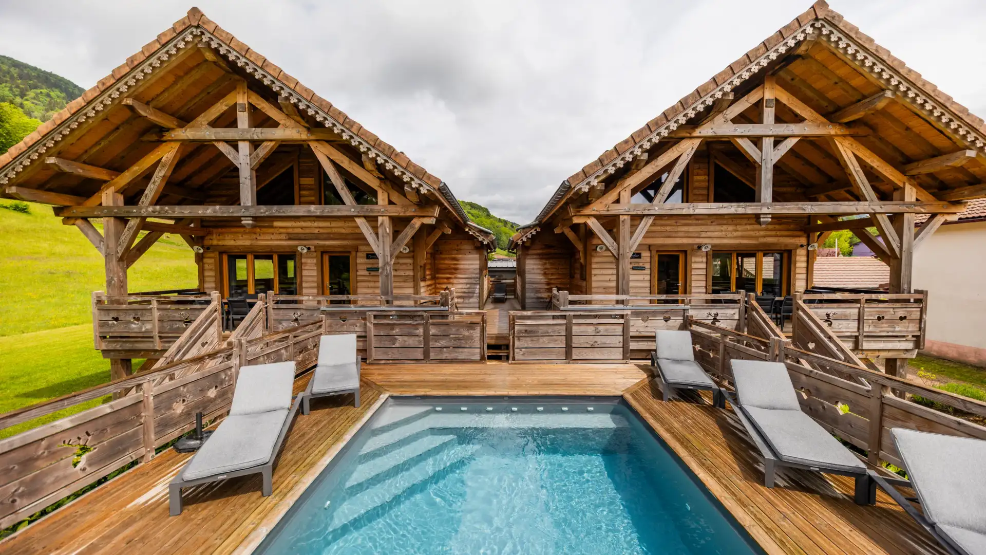 Deux cabanes en bois avec terrasses et un bassin d'eau entouré de transats sur une plateforme en bois