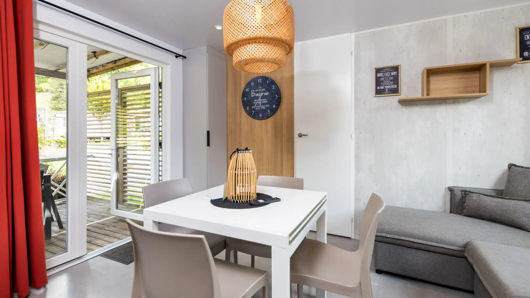 Modern dining room with white table, gray chairs, wicker pendant light, and French door opening onto a terrace.