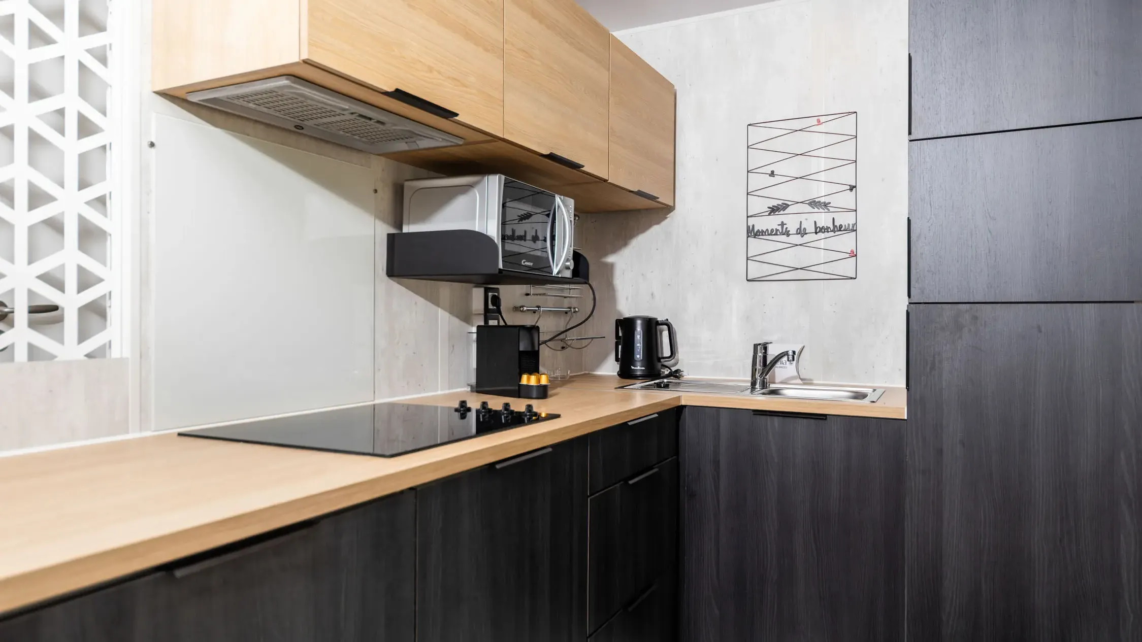 Modern kitchen with light wood worktop, hob, microwave, kettle and a sink under an extractor hood.